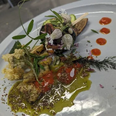 A plated meal garnished with leaves, flowers and sauce.